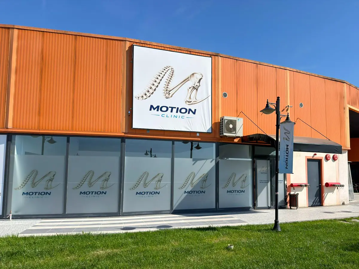 Fațada Motion Clinic văzută într-un unghi lateral: panou portocaliu, vitrine și trotuar spre intrare, Snagov Plaza.