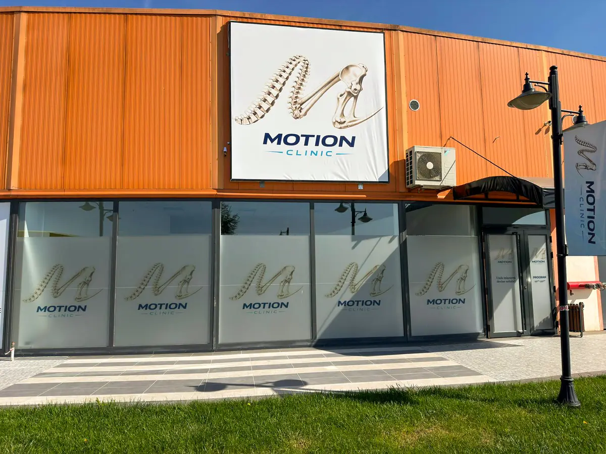 Fațada Motion Clinic în soare — logo pe panou, vitrine cu folie sablată, intrare cu copertină și gazon; complex Snagov Plaza, Ilfov.