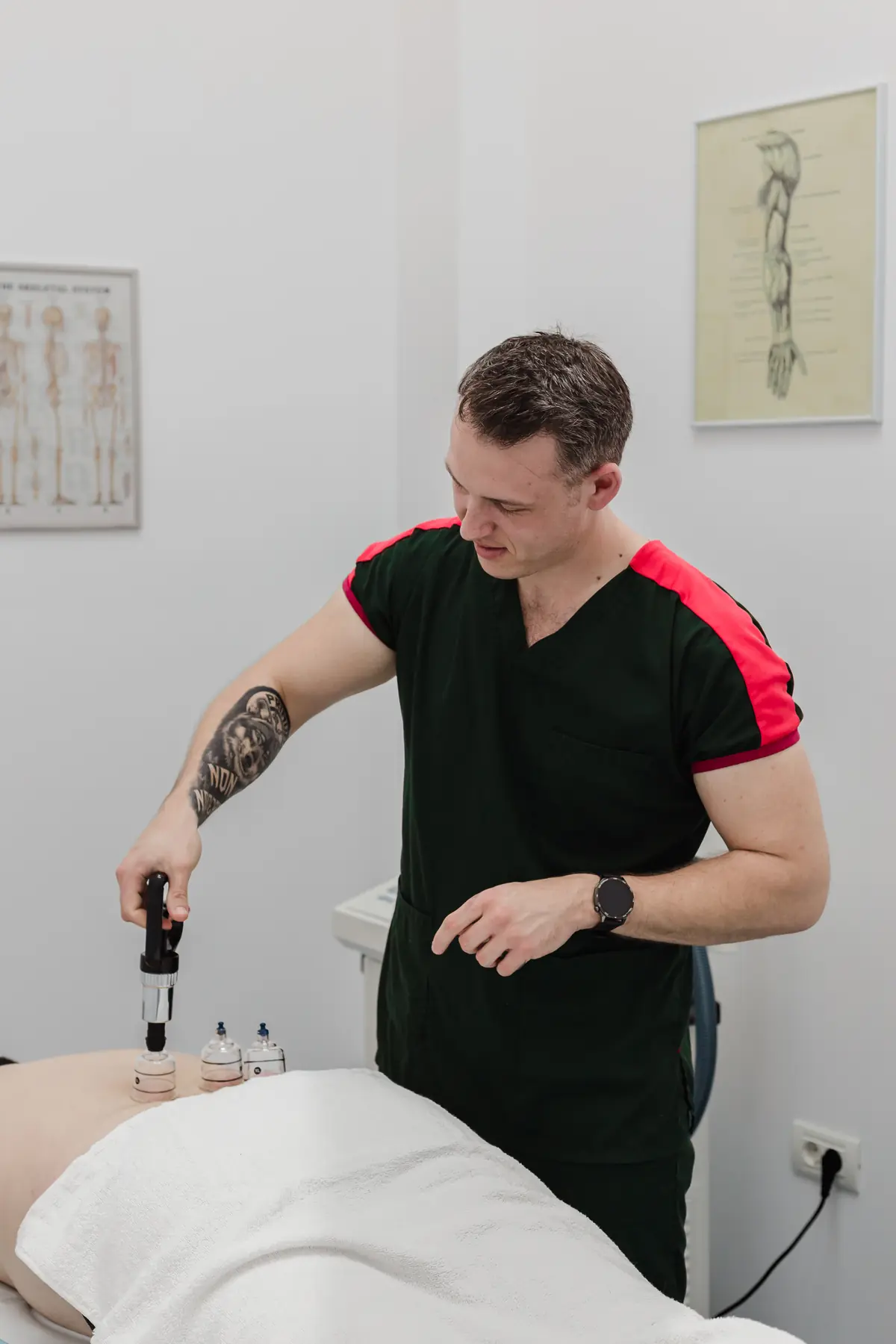 Fizioterapeut Motion Clinic aplică ventuze transparente pe zona lombară a unui pacient întins pe masă; pereti albi cu pliante anatomice în fundal — Snagov Plaza, Ilfov.