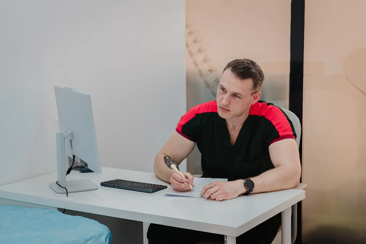 Kinetoterapeut Motion Clinic ia notițe la birou lângă un PC all-in-one; în spate geam sablat cu desen de coloană vertebrală — cabinet consultații, Snagov Plaza.