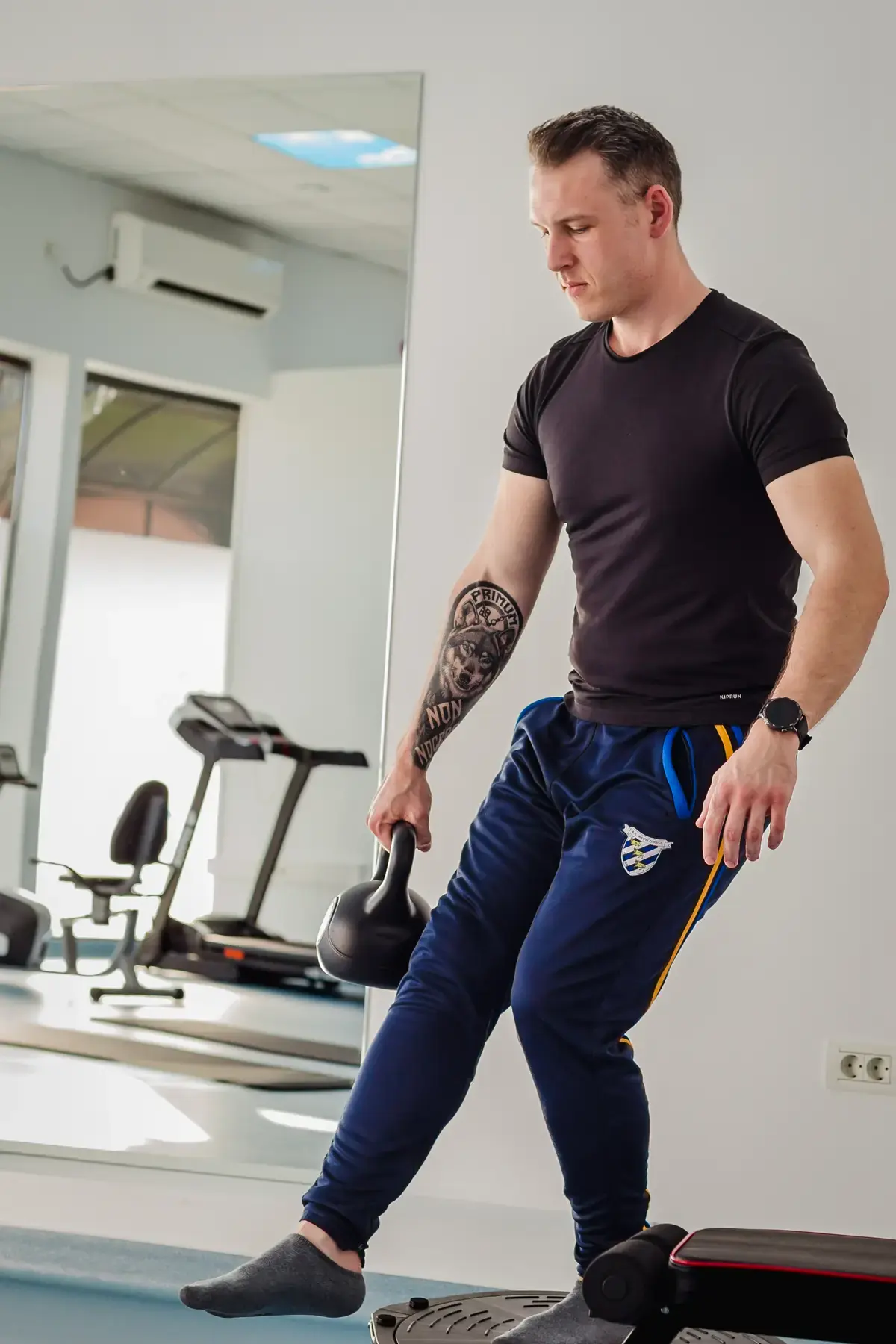 Pacient menține echilibrul pe platformă instabilă pentru antrenament, cu un kettlebell în mână, în sala de exerciții kinetoterapie Motion Clinic, Snagov Plaza, Ilfov.