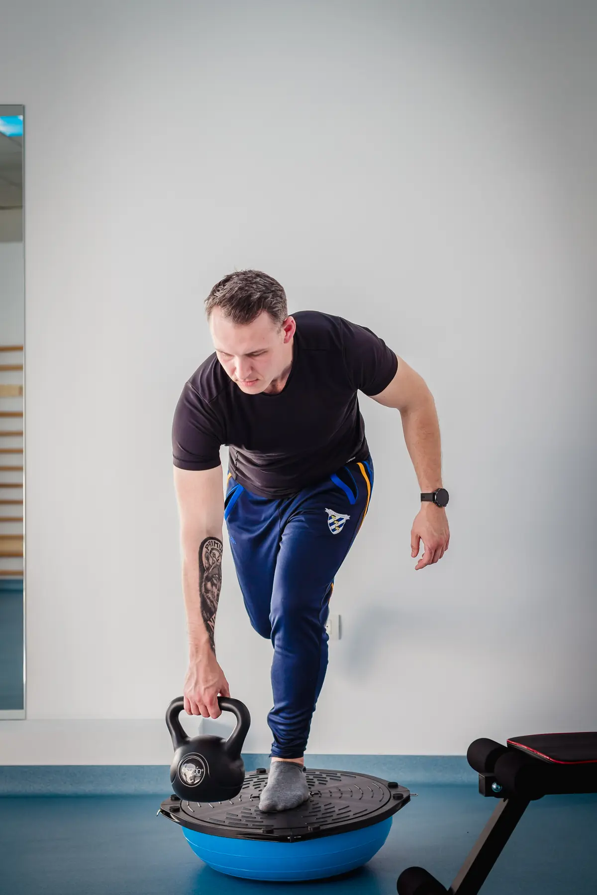 Exercițiu de echilibru pe semisferă cu kettlebell în sala de kinetoterapie Motion Clinic, față în oglindă — Snagov Plaza, Ilfov.
