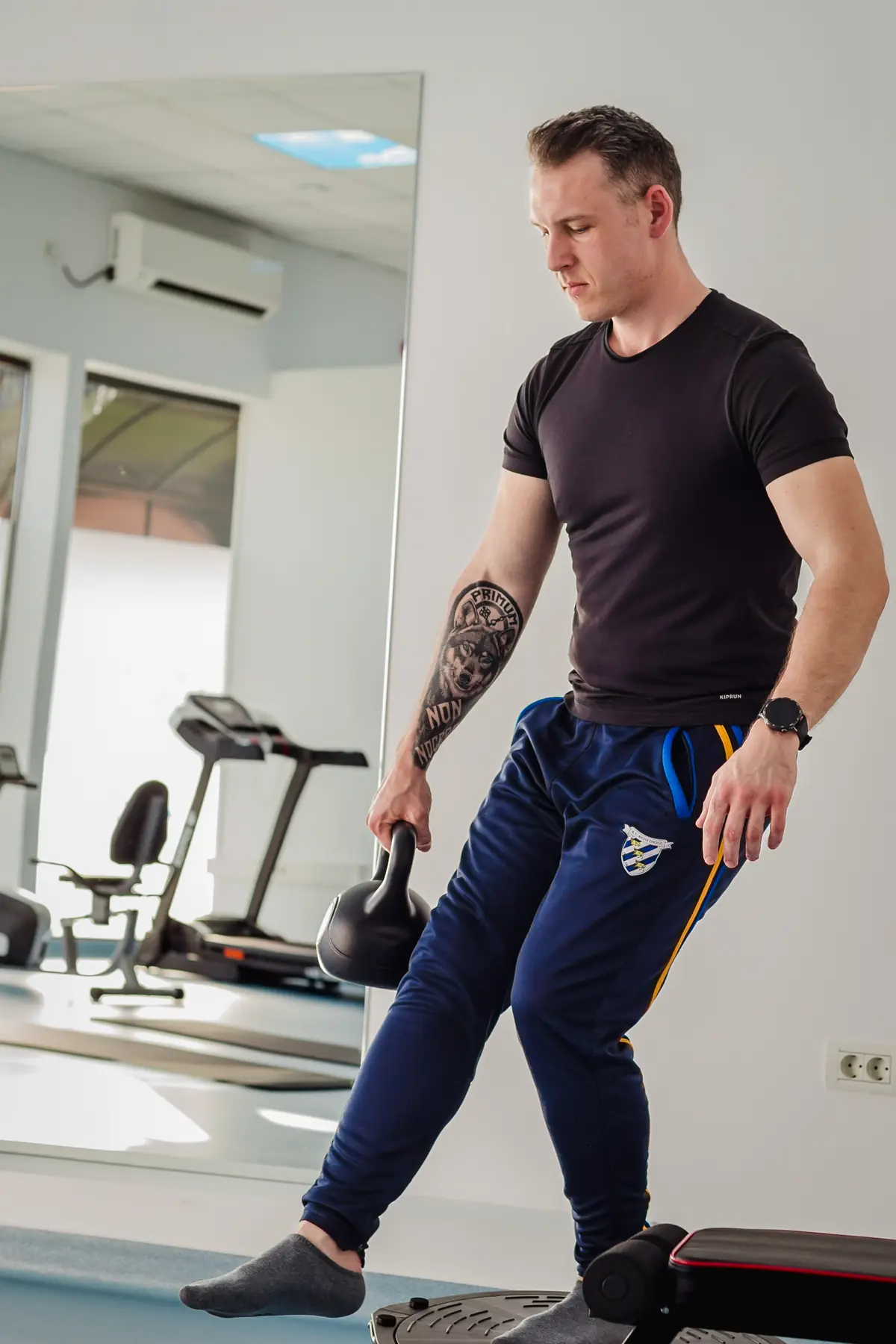 Pacient pe platformă circulară cu kettlebell, membru în prelungire — antrenament controlat în sala de exerciții Motion Clinic, Snagov Plaza.