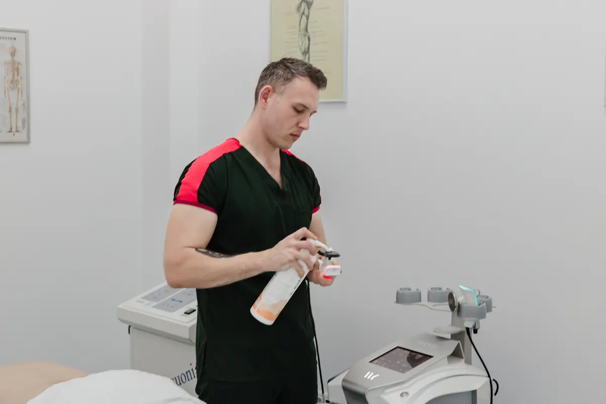 Terapeut pregătește aplicatorul cu gel conductor în fața consolei tactile; masă de tratament și postere anatomice — Motion Clinic, Snagov Plaza.